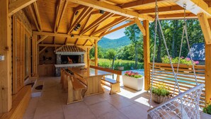 Une cabane en bois comprenant une cuisine, un coin repas et une terrasse avec un fauteuil suspendu.
