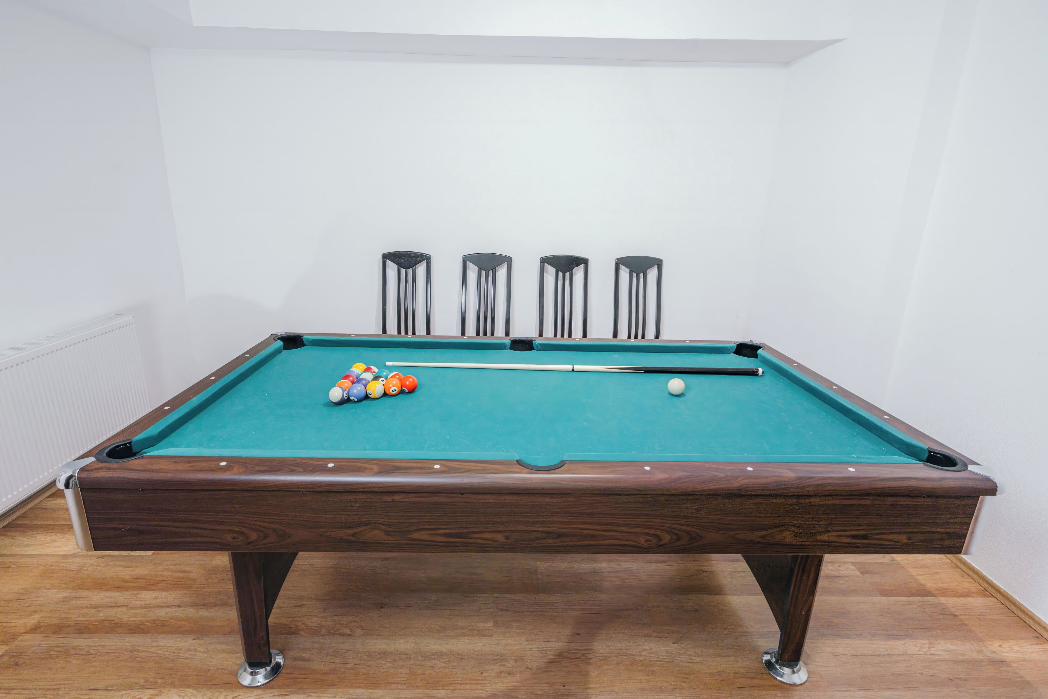 Una mesa de billar con bolas y tacos, patas de madera y superficie de fieltro verde.