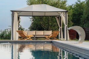 A pool area with a gazebo, two wooden lounge chairs, and a table. - Slavonian home with pool, jacuzzi, barbecue and family fun (Požega)