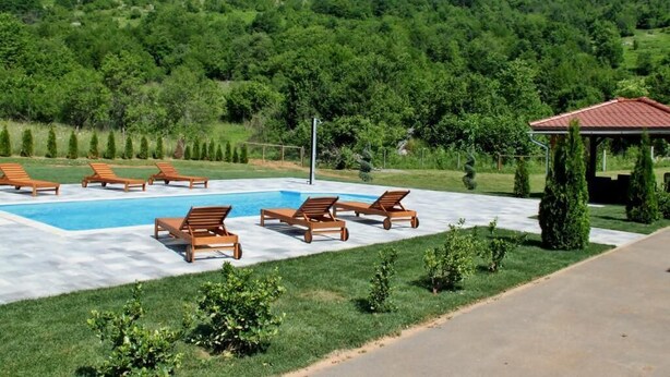 Un área de piscina con sillas de descanso, un pabellón y vistas a una ladera boscosa.