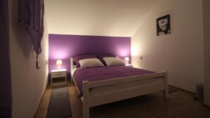 Un dormitorio con cama, mesitas de noche, lámpara y una obra de arte en la pared.