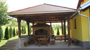 Un espacio al aire libre cubierto con una chimenea de ladrillo, muebles de madera y un edificio amarillo al fondo.
