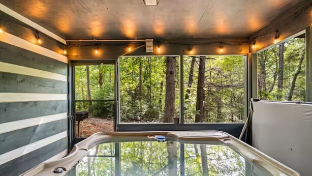 A modern cabin with a glass-enclosed hot tub, large windows offering forest views, and a rustic wooden interior. - Little Toasty / 9 min to Dollywood! 8 min to Pkwy! (Pigeon Forge)