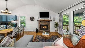 A living room with a fireplace, a dining area with blue cabinets, and a TV mounted on the wall. - Little Toasty / 9 min to Dollywood! 8 min to Pkwy! (Pigeon Forge)