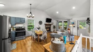 A spacious living area with a fireplace, a dining table with patterned chairs, and a kitchen with modern appliances. - Little Toasty / 9 min to Dollywood! 8 min to Pkwy! (Pigeon Forge)