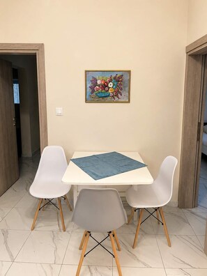 Ein Essbereich mit einem weißen Tisch, zwei weißen Stühlen, einer blauen Tischmatte und einem farbenfrohen Bild an der Wand.