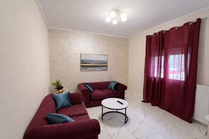 Un salon avec deux canapés rouges, une petite table ronde, un tableau accroché au mur et une fenêtre ornée de rideaux rouges.