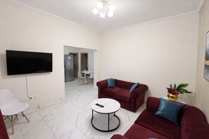 Ein modernes Wohnzimmer mit einem Flachbildfernseher, roten Sofas mit blauen Kissen, einem weißen Couchtisch und einem kleinen Beistelltisch mit einer Pflanze.