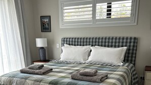 A neatly made bed with a checkered bedspread, two pillows, and two folded towels. There is a window with blinds, a bedside lamp, and a framed picture on the wall. - Private attractive single story bungalow, sleeping 4 people. (Redwood Valley)