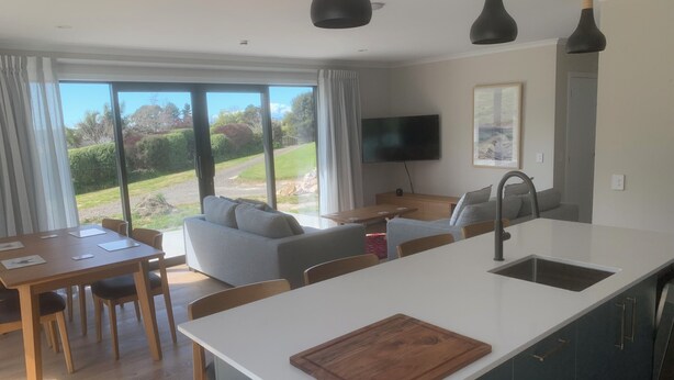 A modern kitchen with a central island, dining area with wooden table and chairs, and a living area with a sofa and TV. - Private attractive single story bungalow, sleeping 4 people. (Redwood Valley)
