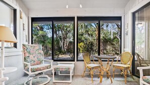 A room with a large window, two wicker chairs, a small table, and a white armchair. - Monthly Coastal Retreat | Garage, Pools, Beach Access & Quiet Community (New Smyrna Beach)