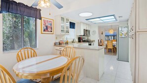 A kitchen with white cabinets, a microwave, and a refrigerator. There is a dining area with a wooden table and chairs. - Monthly Coastal Retreat | Garage, Pools, Beach Access & Quiet Community (New Smyrna Beach)