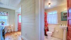 A room with wooden floors, a bed, a chair, a window with artwork, and a pink door.