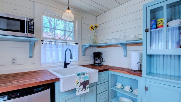 A kitchen with a white sink, a microwave, a coffee maker, and a cabinet with dishes.