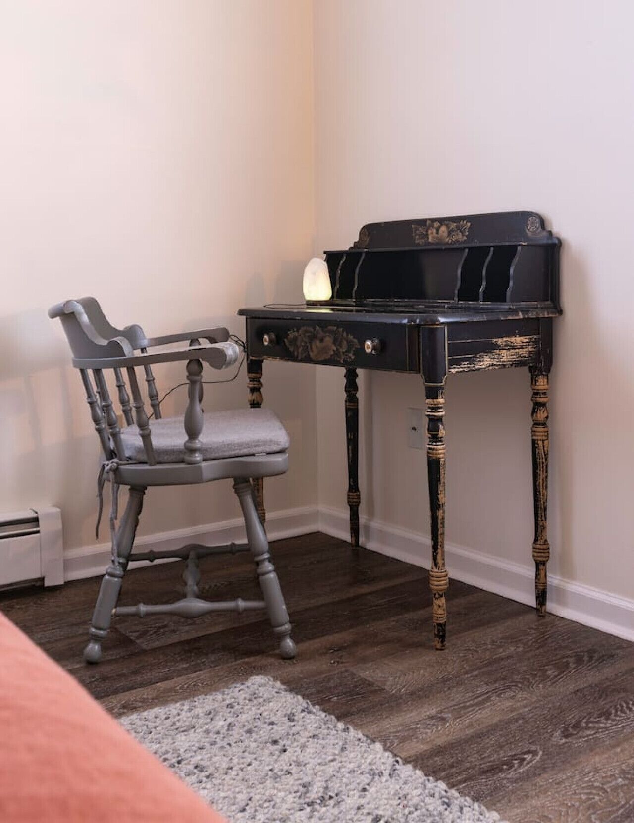 A room with a dark wooden desk, a grey upholstered chair, and a small vase on the floor.