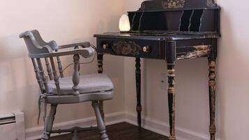 A room with a dark wooden desk, a grey upholstered chair, and a small vase on the floor.