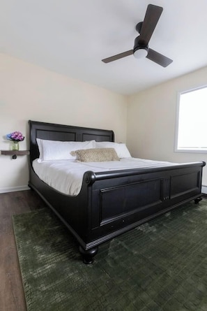A bedroom with a black bed, a ceiling fan, a green rug, and a window.