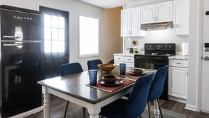 Una cocina moderna con armarios blancos, un refrigerador negro y una zona de comedor con sillas azules y una mesa de madera.