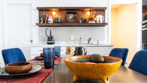 Una cocina moderna con una mesa de comedor de madera, sillas azules y un colorido centro de mesa en un bol.