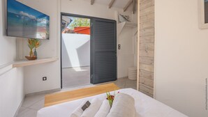 Ein modernes Schlafzimmer mit Bett, einem an der Wand montierten Fernseher und einer Schiebetür zu einem Außenbereich.