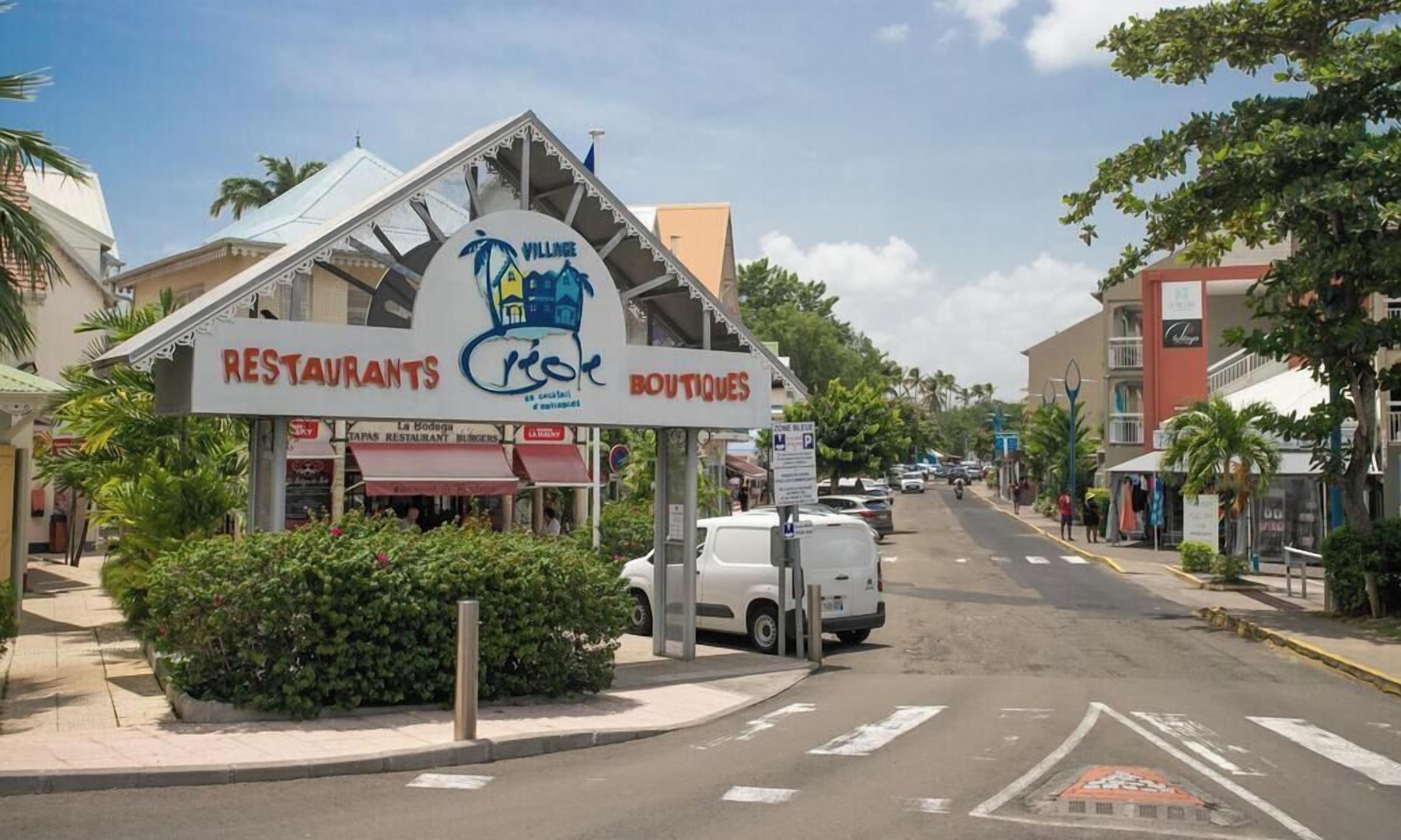 A street view with a sign for 'VILLAGE RESTAURANTS' and 'BOUTIQUES' with a building in the background.