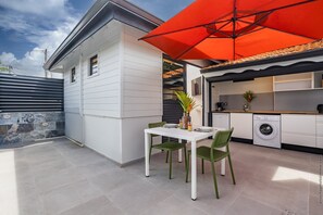 A modern kitchen with white cabinets, a washing machine, and a dining area with a table and chairs. - Bungalow PunchCoco - Beachfront (Les Trois-Îlets)
