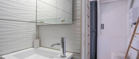A modern bathroom with a white sink, chrome faucet, and a glass shelf above the mirror.