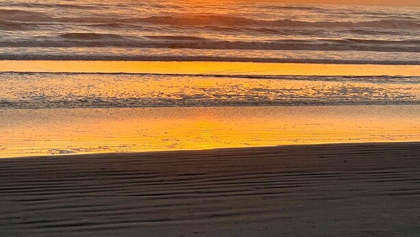 Een strand bij zonsondergang, met golven en een heldere lucht.