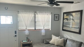 Een woonkamer met een grijze bank, een kleine tafel met een lamp en een plafondventilator.