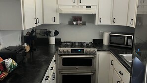 Een moderne keuken met witte kasten, een gasfornuis, een oven, een magnetron en een koelkast.