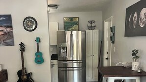 Een kleine keuken met een koelkast, een eettafel met stoelen en een gitaar die tegen de muur staat.