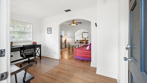 Una habitación amplia con pisos de madera, un escritorio con silla, una mesa de comedor con sillas y un sofá colorido.