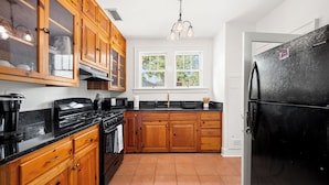 Cocina con armarios de madera, un refrigerador negro y un ventanal con vista a árboles.