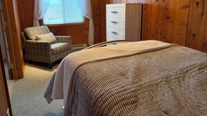 A bedroom with a bed, a chair, a wardrobe, and a window with curtains.