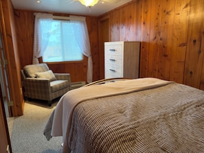 Une chambre à coucher avec un lit, une chaise, une armoire et une fenêtre avec des rideaux.