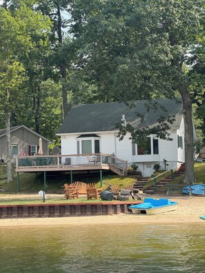 A house with a deck, a covered area, and a boat docked on the shore.