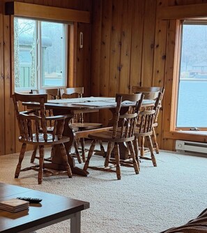 A wooden interior with a round table and chairs, carpeted floor, and large windows.