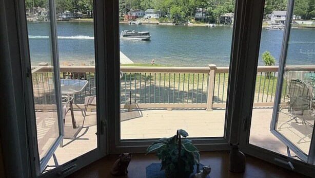 A view from a room with large windows overlooking a lake, a boat, and a dock.