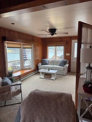 A cozy room with a white sofa, a small coffee table, and a view of a lake through large windows.