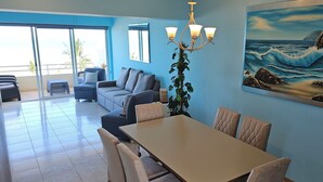 A modern living room with a dining area, large windows, and a coastal painting. - 2-bedroom apartment in peaceful Mazatlán with an amazing front ocean view (Mazatlán)