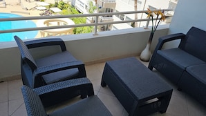 A balcony with wicker furniture, a view of a swimming pool, and a railing with a vase and scissors. - 2-bedroom apartment in peaceful Mazatlán with an amazing front ocean view (Mazatlán)