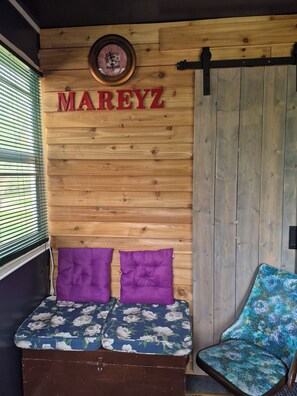 A room with a wooden wall, a bed with purple pillows, a chair with a floral pattern, and a clock with the name 'MAREYZ' on the wall.