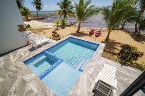 Ein Pool mit klarem, blauem Wasser, eine weiße Liege und Blick auf Strand und Meer.