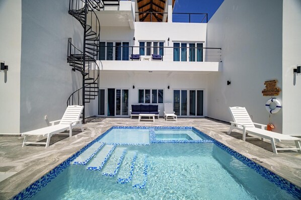 Ein Pool mit blauen Mosaikfliesen, weißen Liegestühlen und einer Wendeltreppe.
