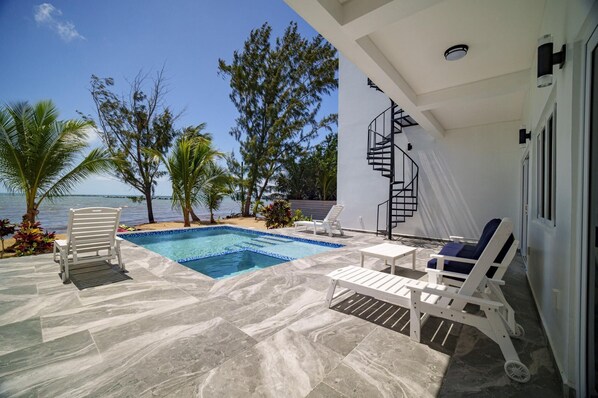 A pool area with a clear view of the sea, a white outdoor seating area, and a spiral staircase leading to an upper level.