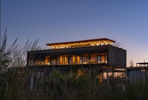 Una casa moderna de dos pisos con balcón, ventanas grandes y luces colgantes.