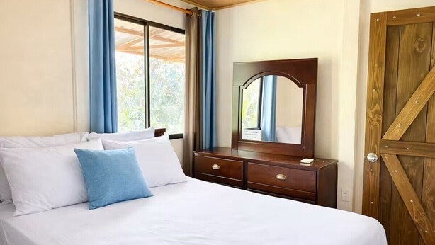 Ein Schlafzimmer mit Bett, Kommode, Spiegel und Holztür.