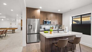A modern kitchen with a stainless steel refrigerator, wooden cabinets, a marble countertop, and a large window.