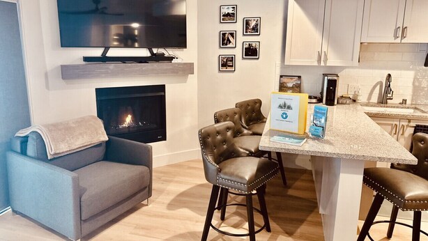 Una sala de estar moderna con televisión de pantalla plana, chimenea, sofá y zona de comedor con taburetes de bar.