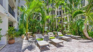 A courtyard with lounge chairs, potted plants, and a building facade. - Palm Breeze Palm Beach Island Studio Heated Pool (Palm Beach)